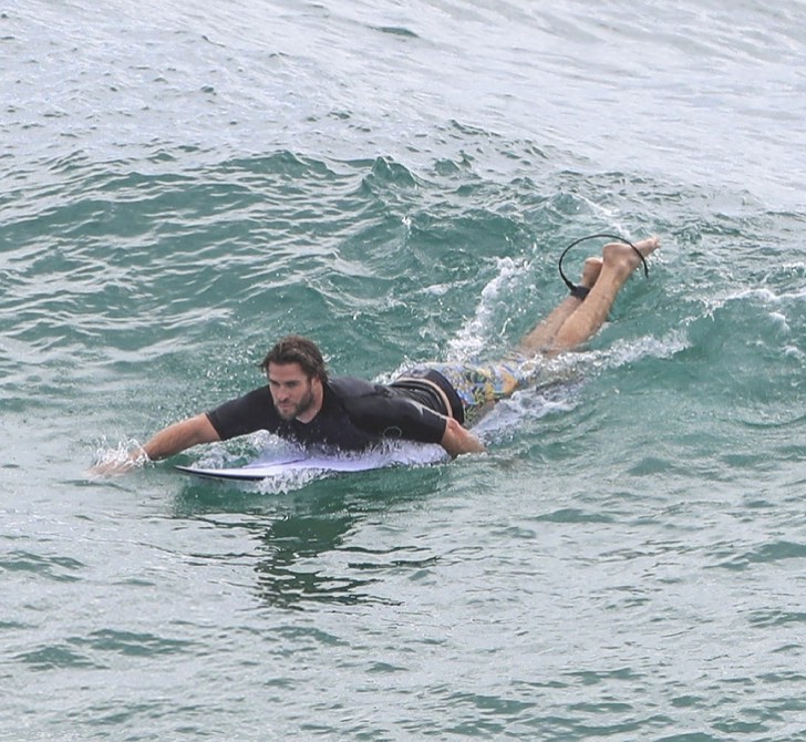 Киноактер Лиам Хемсворт плывет на доску для сёрфинга.