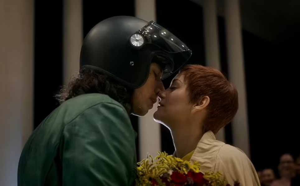 Актер Адам Драйвер в мотоциклетном шлеме целуется с девушкой.