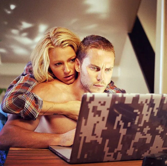 Актер Тейлор Китч смотрит в ноутбук. Его обнимает девушка.